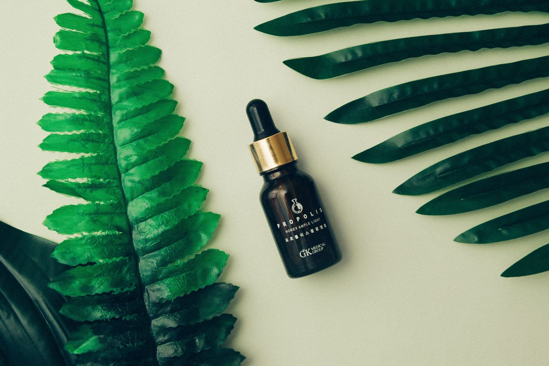A green leaf and a clear serum dropper on a neutral background