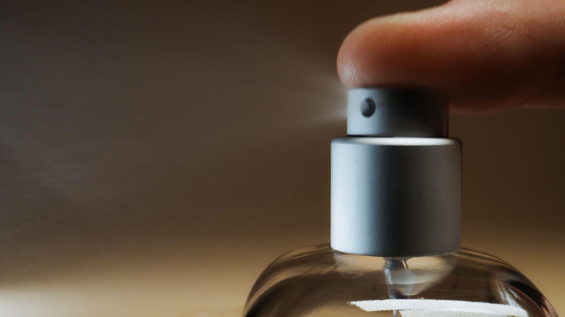 A finger pressing the pump of a fragrance spray bottle