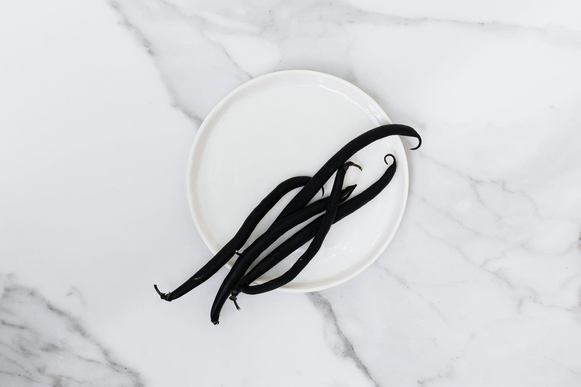 Vanilla pods on a white plate on marble