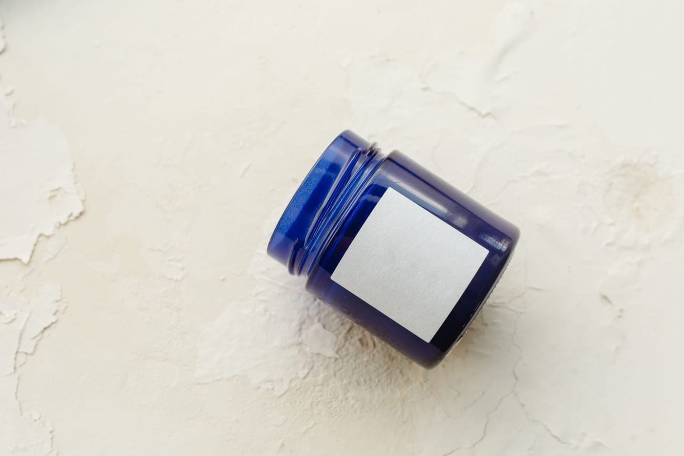 A cobalt glass cream jar with a blank label on a pale plaster surface