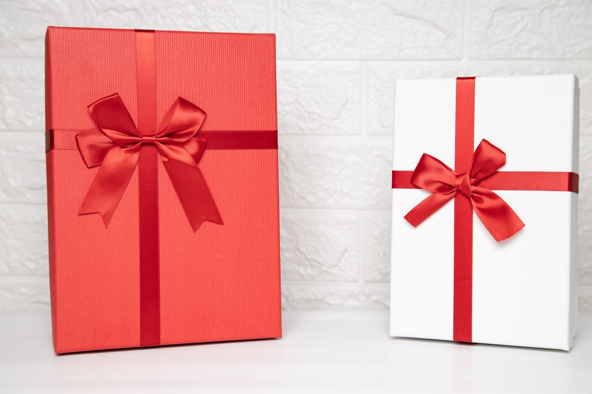 Two wrapped gift boxes with red ribbon on a pale surface