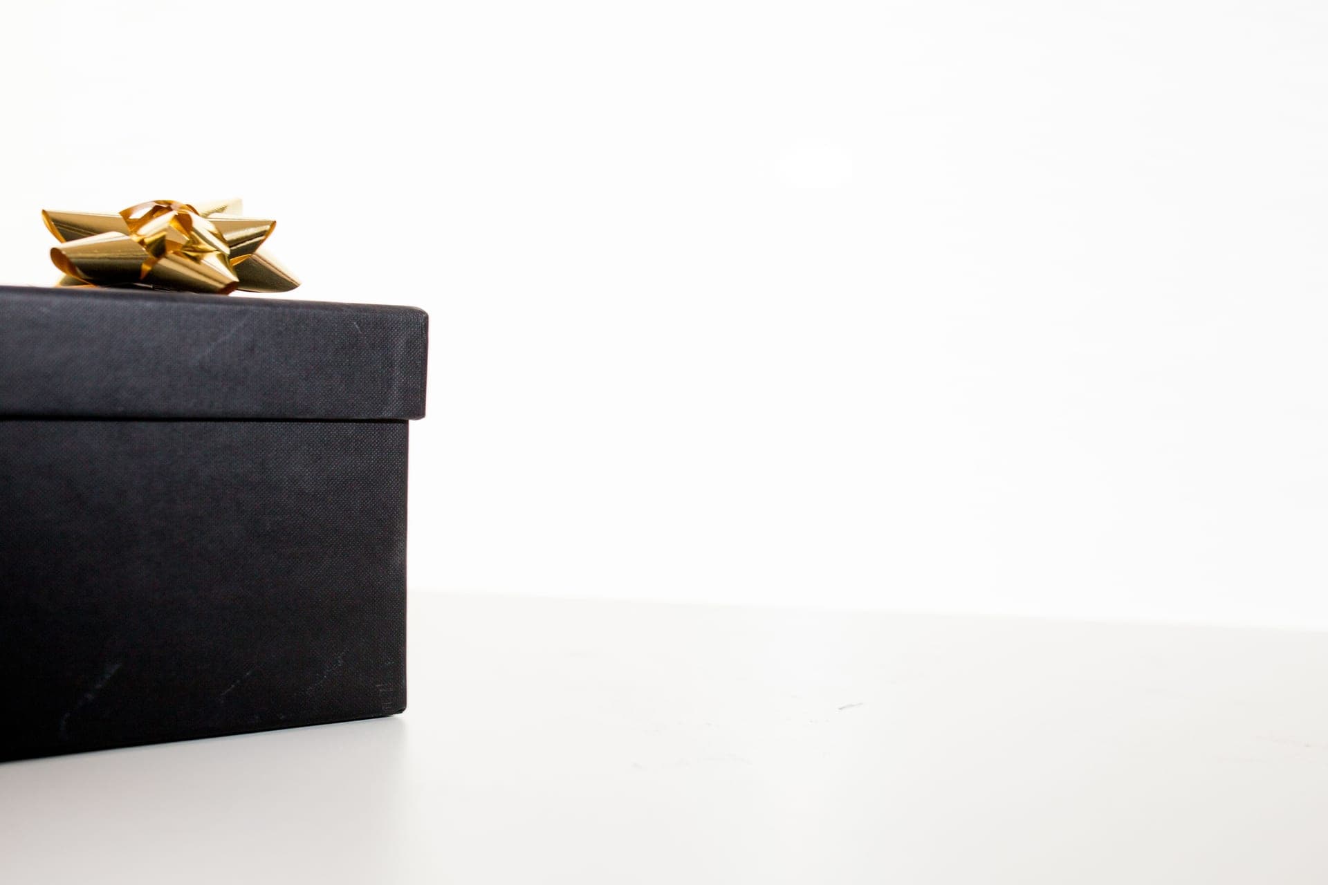 A black gift box with a gold bow on a pale surface