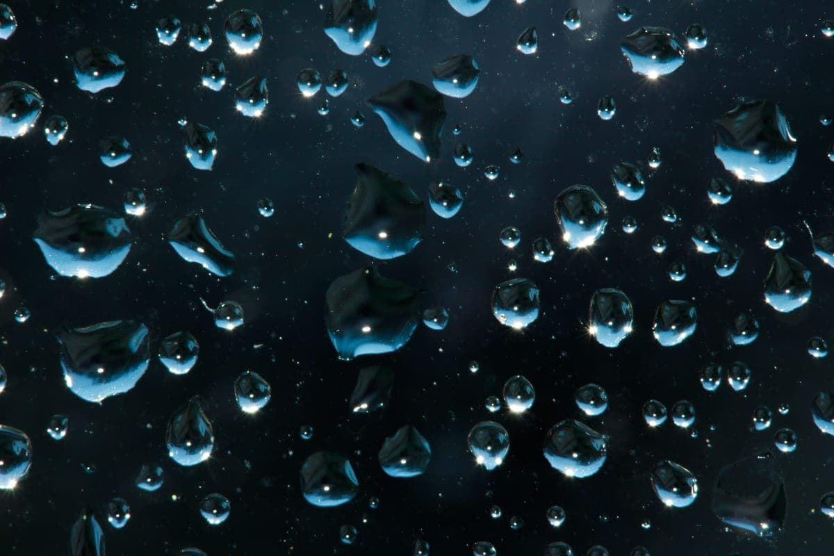 Beads of water on a dark glass surface, side-lit