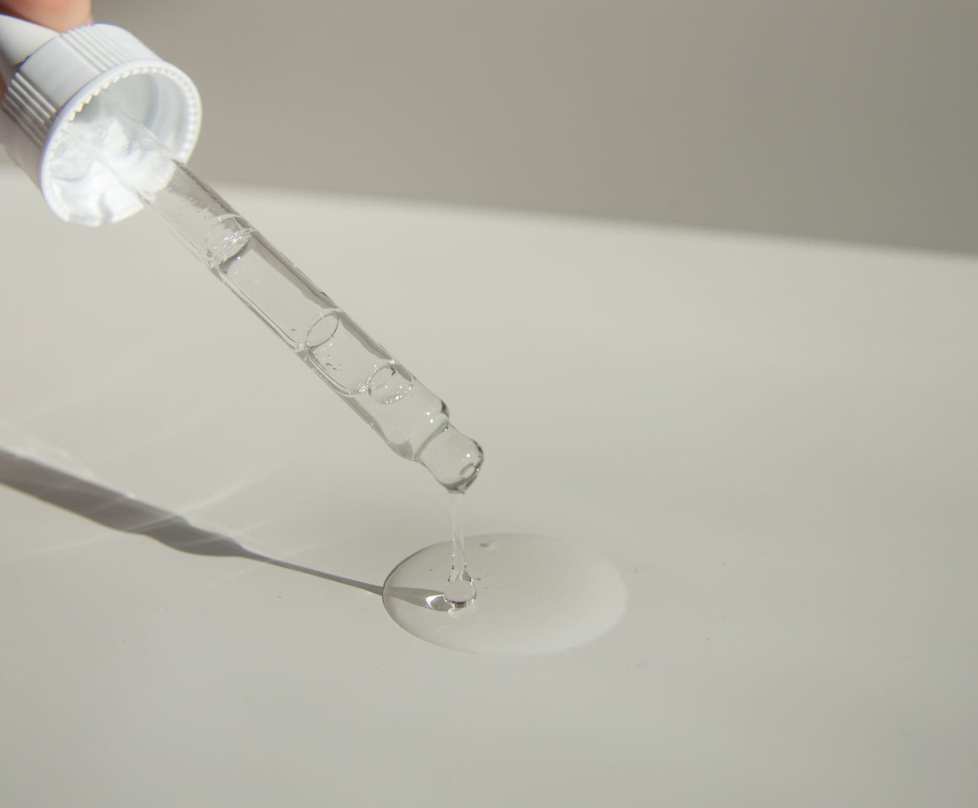 A clear serum bottle with a dropper on a pale surface