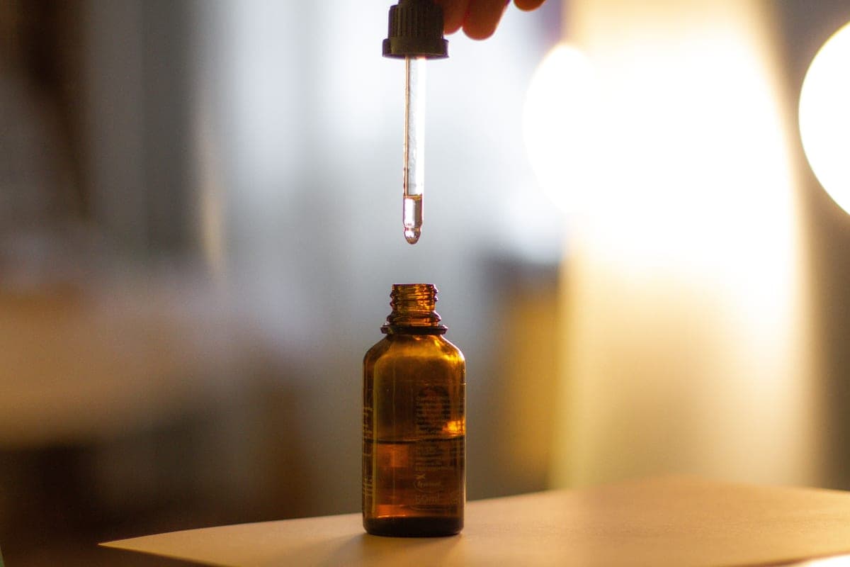 Amber glass serum bottle with a dropper on a dark surface, lit from one side