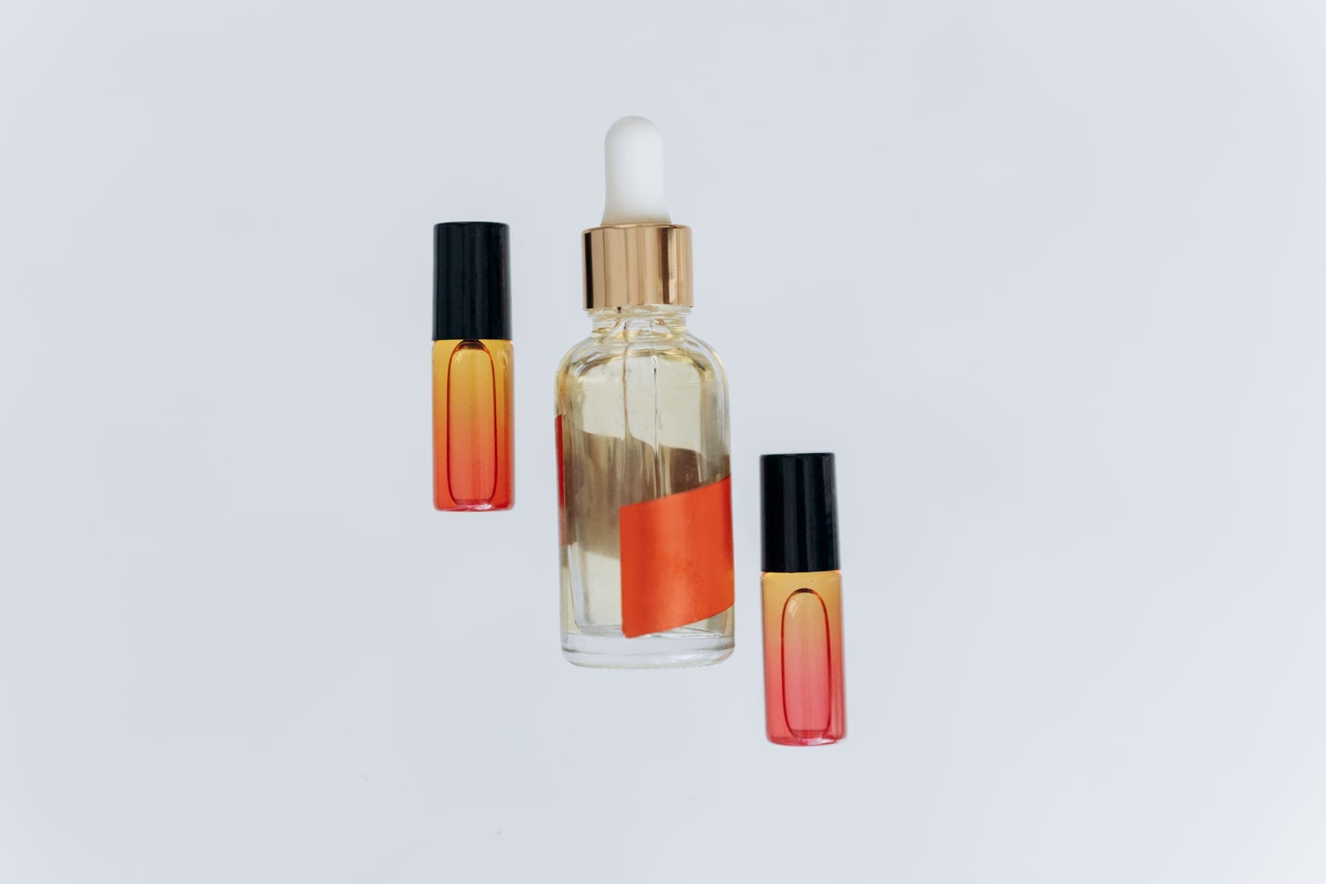 A clear glass dropper bottle and two roll-on vials on a pale background