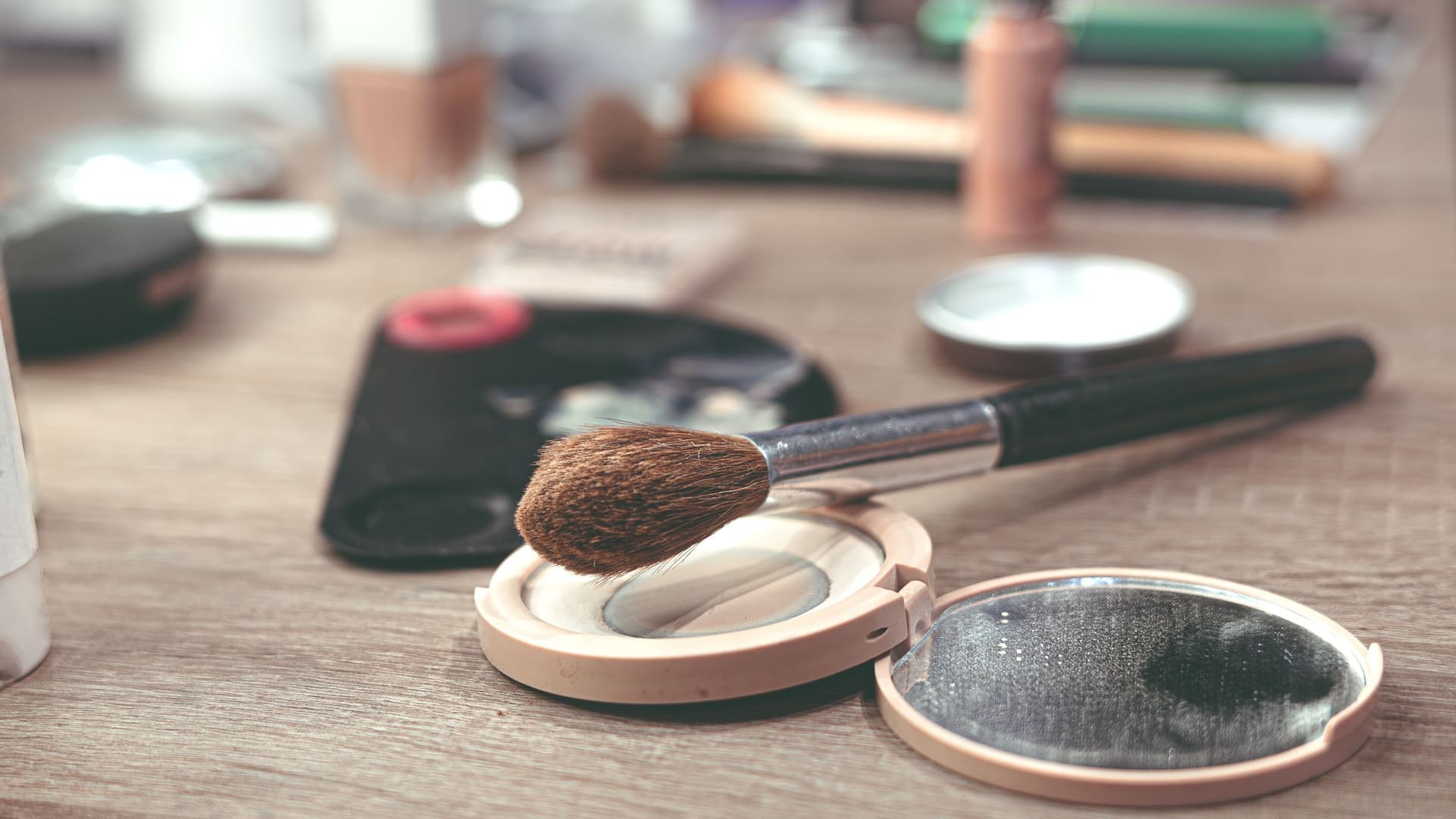 Makeup brushes and a compact of powder on a wooden table