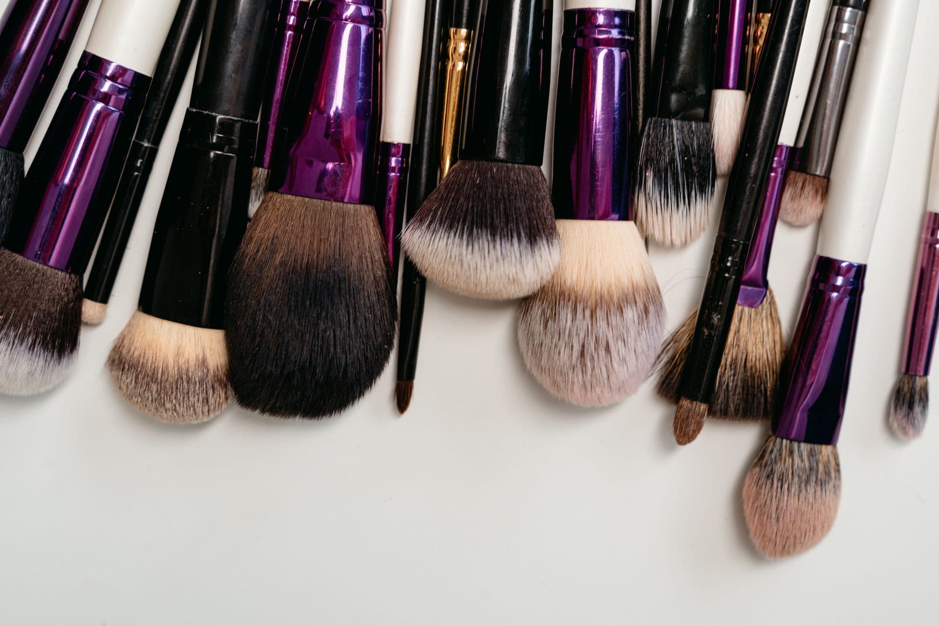 A row of makeup brushes laid on a pale surface