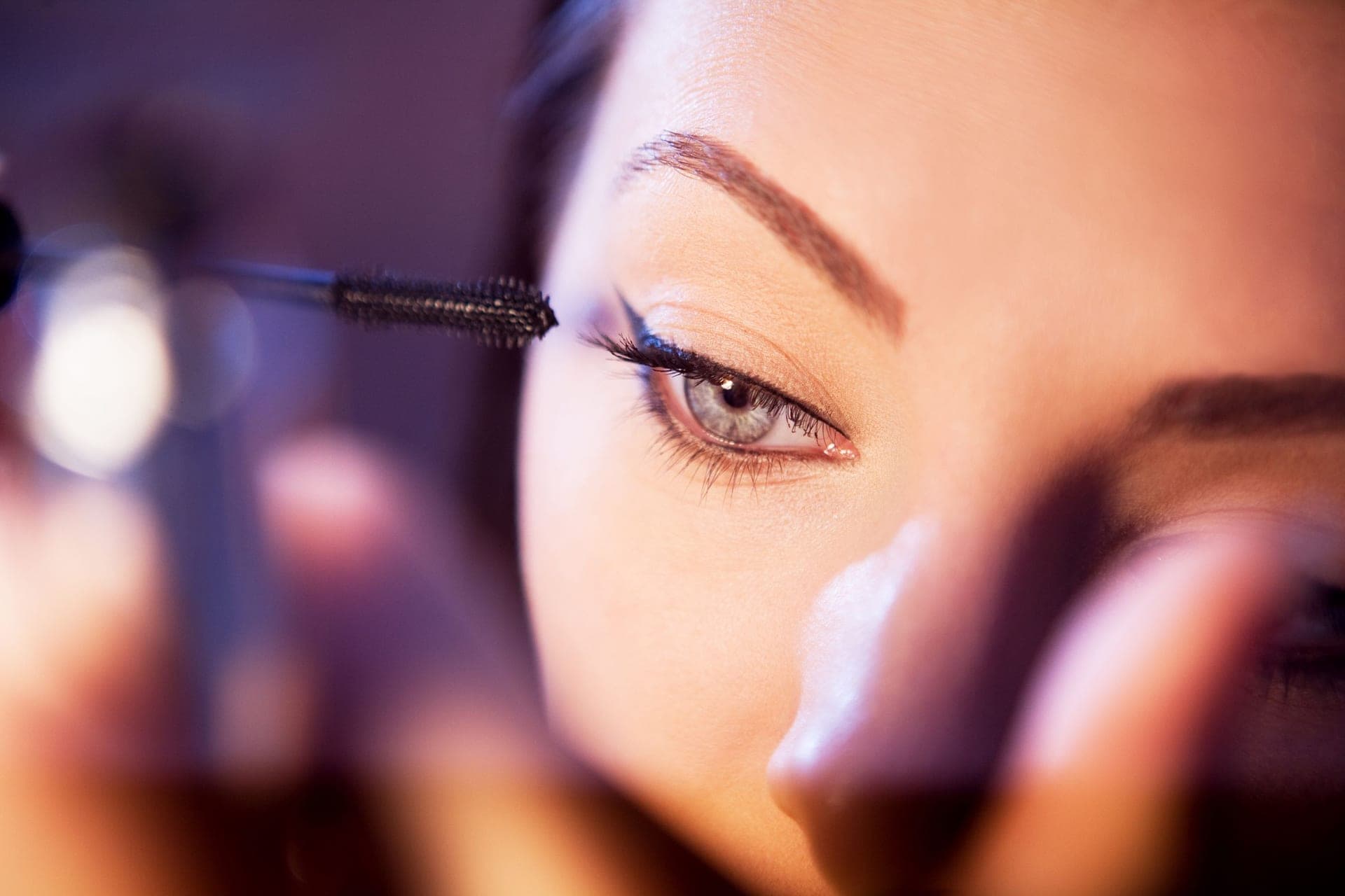 A close-up of eyelashes with a mascara wand