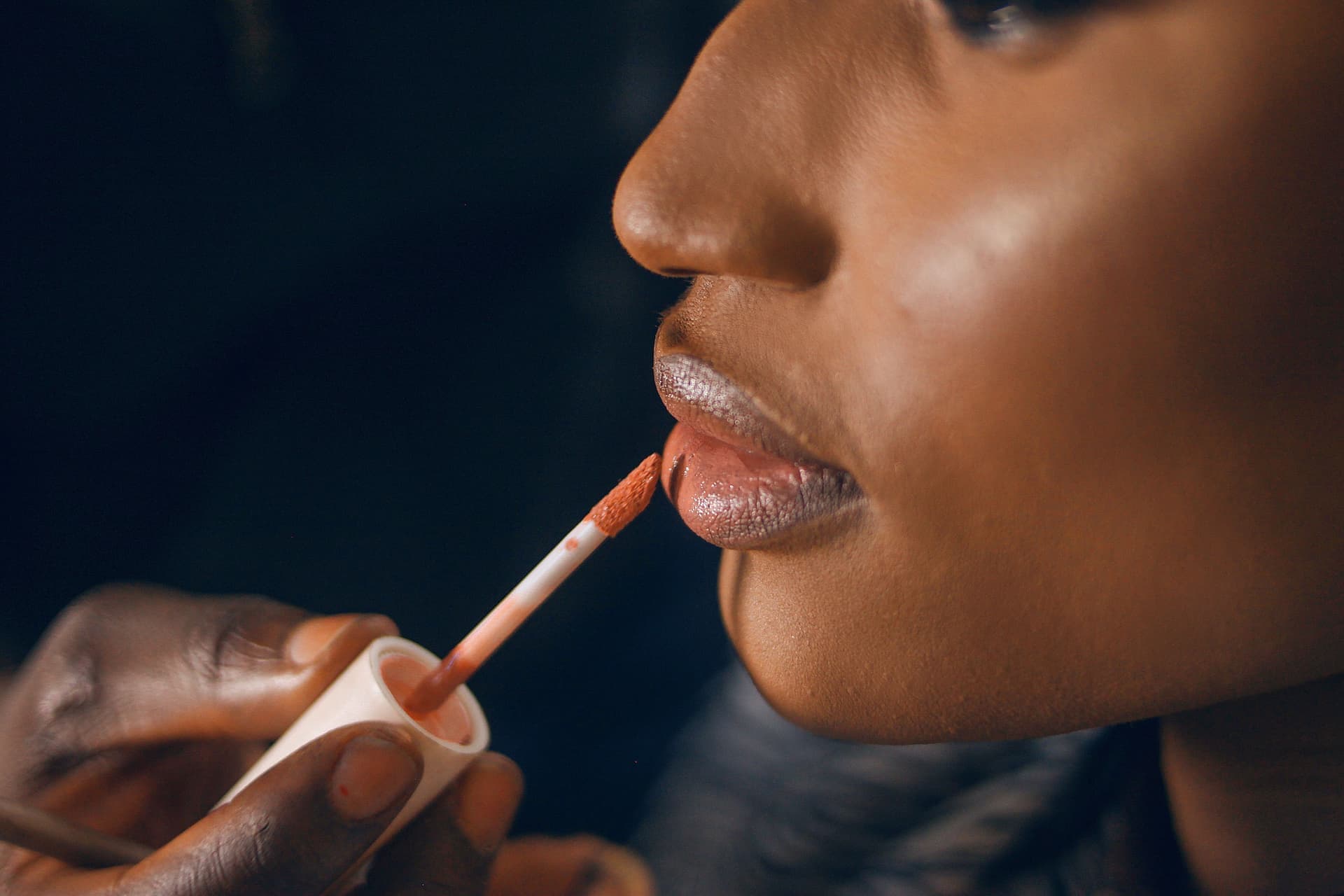 A person applying a glossy lip product with a doe-foot applicator