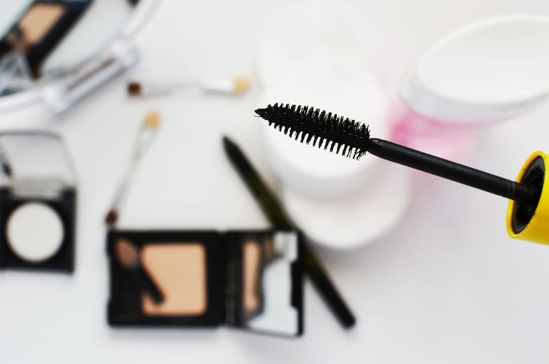 A mascara wand beside compact makeup