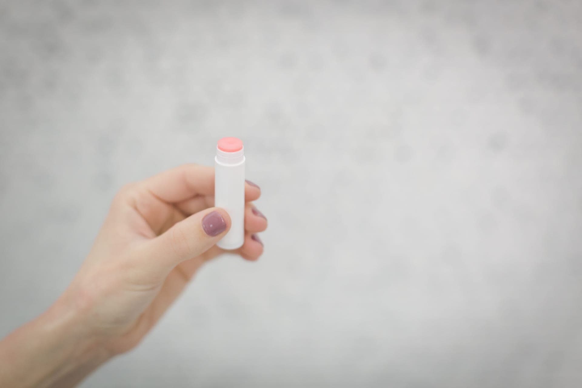 A hand holding a white lip balm tube