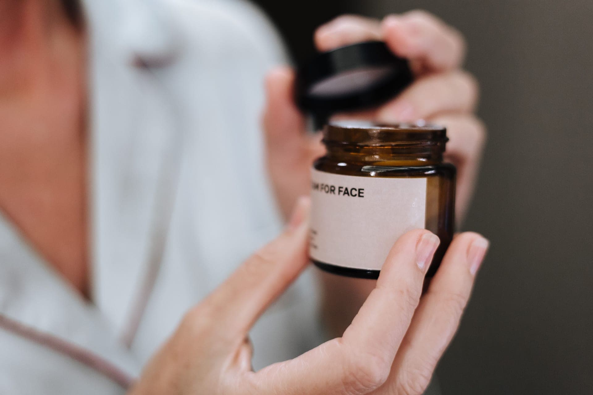 A person opening an amber jar of face cream