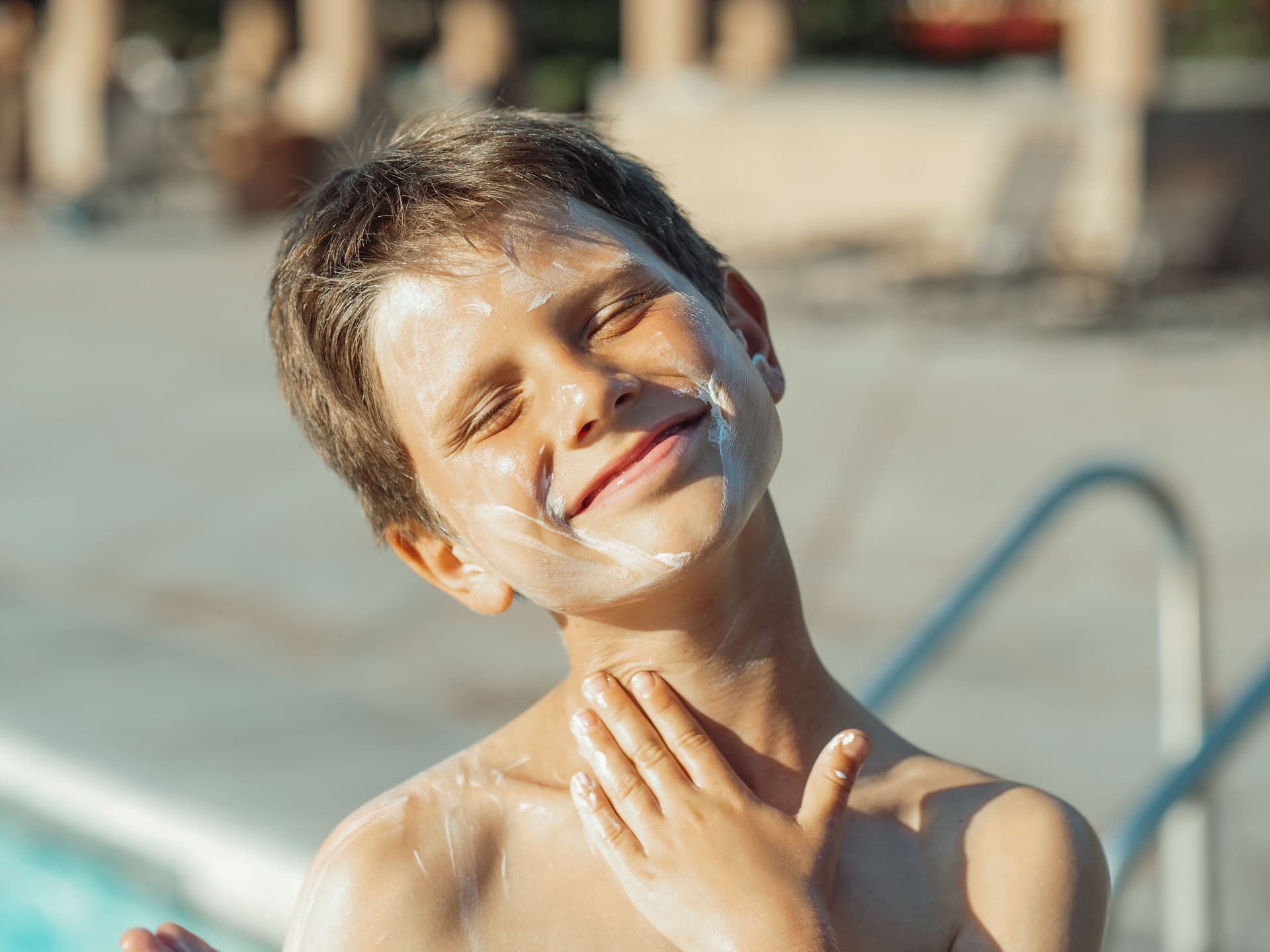 A child with sunscreen on their face beside a pool