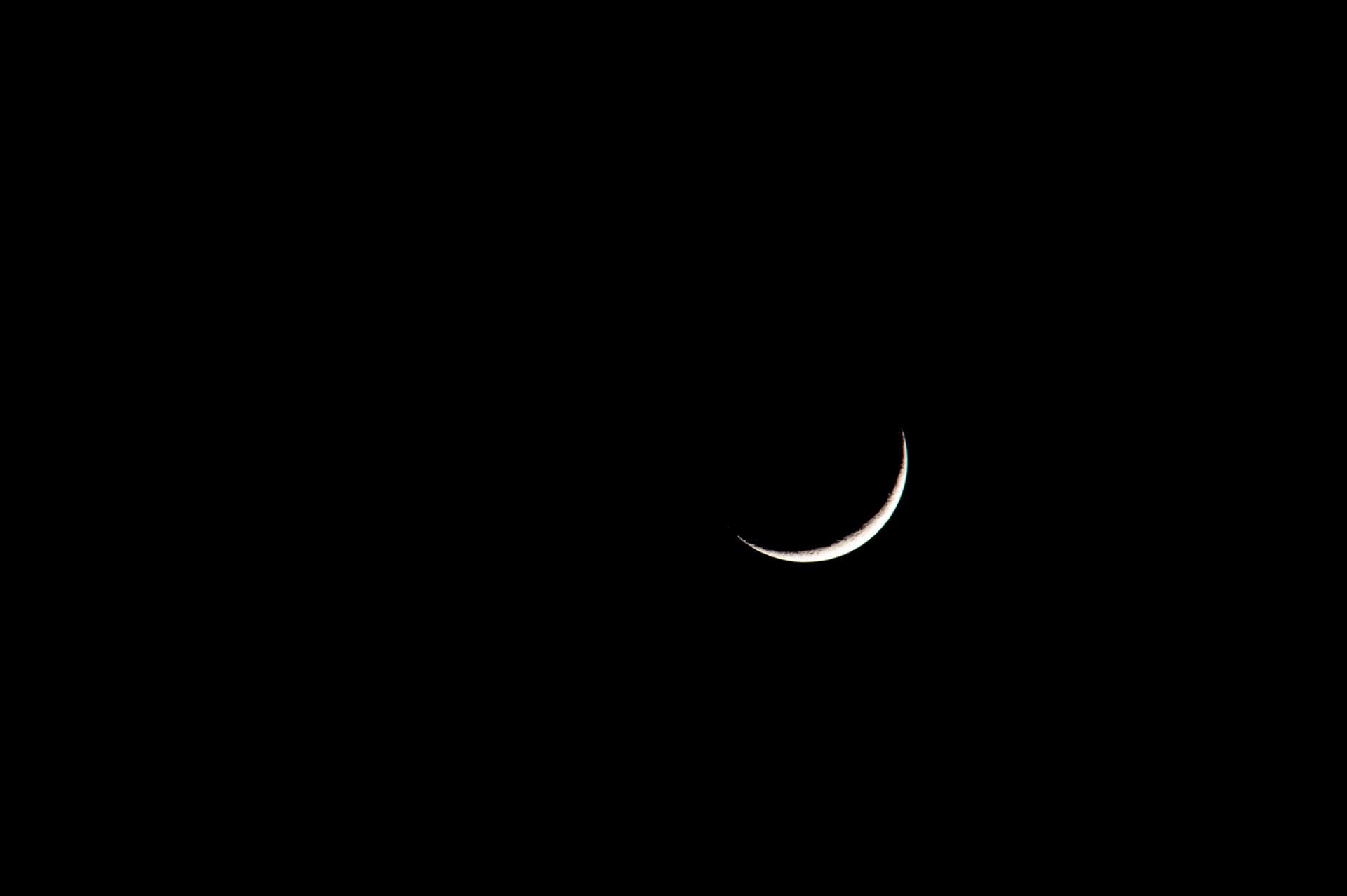 A thin crescent moon in a black night sky