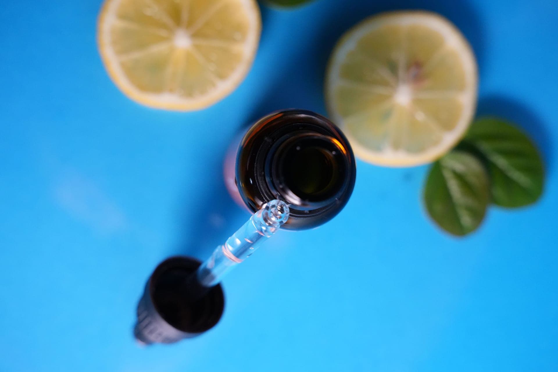 A serum dropper above an amber bottle with citrus slices on blue