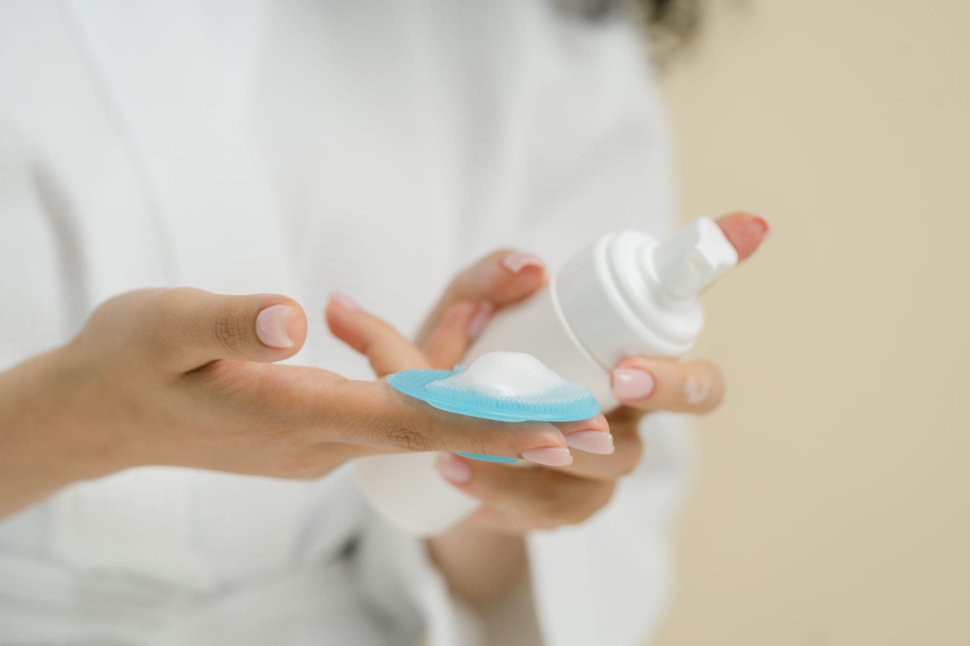 Hands holding a silicone cleansing brush with foaming cleanser